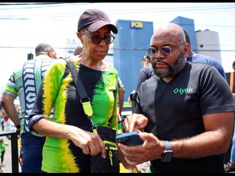 Lynk Chief Executive Officer Vernon James demonstrates to Education Minister Fayval Williams how to use the Lynk app recently.