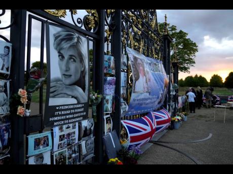The sun rises as people begin to gather in front of portraits and messages of remembrance of Princess Diana displayed on the gates of Kensington Palace, in London, on Wednesday, August 31.