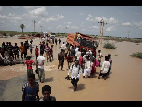 People walk on a flooded road after a heavy rainfall in the village of Aboud in the El-Manaqil district of the Al-Jazirah Province of Sudan recently.
