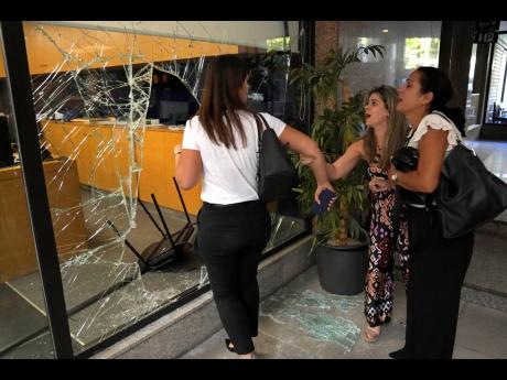 Panicked bank employees stand next to a window that was broken by attackers to exit the bank in Beirut, Lebanon, on Wednesday. 