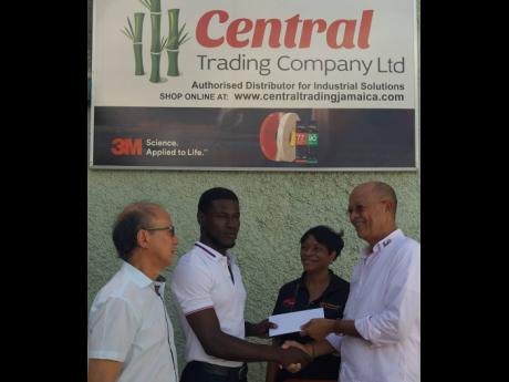 Donald Patterson (right), director, Rotary Club of St Andrew North Education Foundation, hands over a cheque for $100,000 as an education grant to Tarique Barrett, second-year marketing and accounting student at The University of the West Indies. Looking o