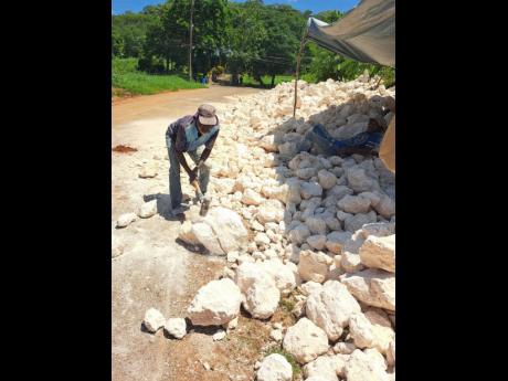 Donald McLean uses a sledgehammer to break rocks near Big Pond in St Catherine on Friday as workmen construct a retaining wall to address the long-standing flooding problem.  Photos by Rasbert Turner