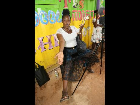 Elaine Escoe points to the slippers that she wears to leave and enter her community in order to protect her ‘church’ shoes, which she takes from her bag, from being damaged by the deplorable condition of the roadway in Redberry, Manchester. 