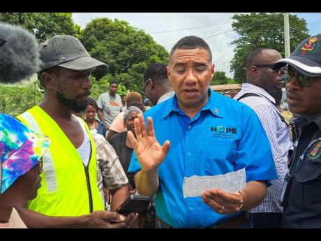 Prime Minister Andrew Holness examines a copy of a receipt received by a resident when he handed over funds to unscrupulous persons selling lands on the outskirts of Clifton in St Catherine during a visit on Friday. The man’s unfinished house was among a