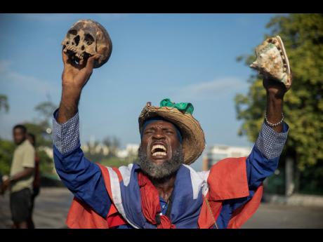 A protester holding up a skull and seashell shouts for the resignation of Haitian Prime Minister Ariel Henry in the street in the Champs de Mars area where the prime minister attended a ceremony marking the death anniversary of revolutionary leader Jean-Ja