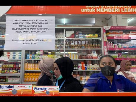 Employees wait for customers at a counter displaying a notification saying that the sale of medicinal syrup is temporarily halted at a pharmacy in Jakarta, Indonesia, Thursday, Oct. 20. Indonesia temporarily halted the sales of medicinal syrups that treat 