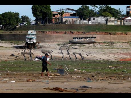 A man walks by boats on dry land in an area impacted by the drought near the Solimões River, in Tefe, Amazonas state, Brazil, Wednesday, Oct. 19, 2022. Months after enduring floods that destroyed crops, thousands of families in the Brazilian Amazon are no