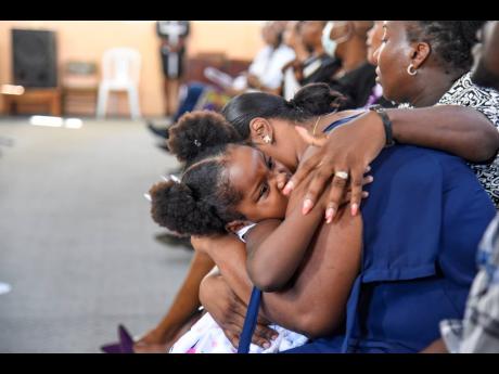Daughter Lola (left) comforts a teary-eyed Vanessa Clarke, mother of Michion Campbell, during a memorial service on Friday for the late Kingston Technical High School student, who was stabbed to death by a schoolmate last month. The service was held at the