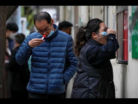 A man looks at his testing tube as a woman gets her routine COVID-19 throat swab at a coronavirus testing site in Beijing, on Thursday, October 27.