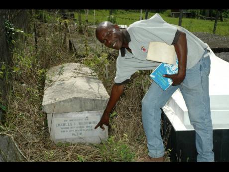 In this September 25, 2006 photo, Fitzroy Chambers, a community historian for Seaford Town, Westmoreland, points to the oldest grave in the Sacred Heart Mission burial plot. Dated March 4, 1928, the plaque bears the name of German descendant Charles Wedemi