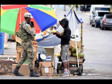 In this June 2020 photo a JDF soldier is seen speaking with a fruit vendor near a checkpoint in Trench Town. 
