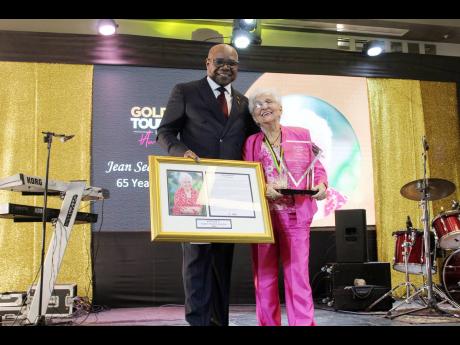 Jean Seaga Anderson, travel agent at Global Travel Services in Mandeville snuggles up to Tourism Minister Edmund Bartletts as she accepts her trophy and citation for 65 years of service in the tourist industry, during the Jamaica Tourist Board’s 2022 Gol
