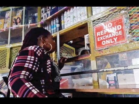 Credit: Photo by Corey Robinson A woman making a purchase at a store in downtown Kingston last week with a prominently placed no refund sign at the cashier.