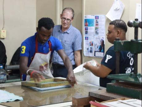 Shawn Jones assists his coworker, Onindia McNamee (left) who is showing Programme officer for the EU delegation to Jamaica,  André Fache how to make recycled paper. 