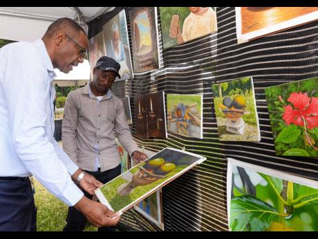 Chief Technical Director in the Ministry of Tourism David Dobson (left), is shown a painting by artist, Damian Cunningham, during the Tourism Product Development Company’s ‘Crafting for Christmas’ fair at Devon House in Kingston on December 16.