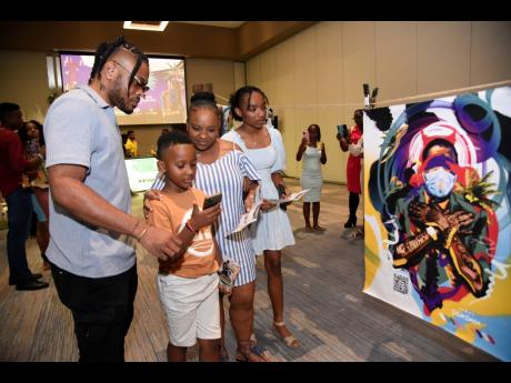 Credit: Nicholas Nunes/Photographer From left: Bonito ‘Don Dada’ Thompson assists Damion Jr, Jhenessa and Jheanell Arnold with scanning his artwork for the ultimate experience.