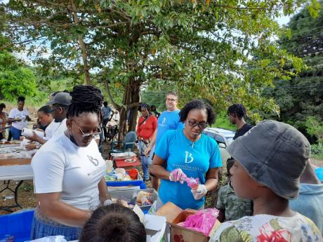 Carmen Hibbert, food and beverage manager and Veniesha Whitely, human resources manager at Bluefields Villas Foundation scoop ice-cream during the Christmas treat. Over 200 children and their parents also received Christmas gifts from the team.