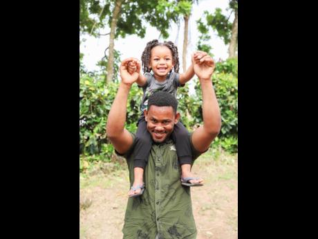 Credit: Contributed Ian Lee Stewart and son, Khalil, are all smiles outside their new home in Ballards, Clarendon.