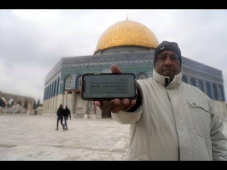 A worshipper stands in the Al-Aqsa Mosque compound in the Old City of Jerusalem, Jan. 29, 2022, and holds his mobile phone showing a threatening message. The May 2021 text, signed ”Israeli intelligence,” reads: “Hello! You have been spotted as having