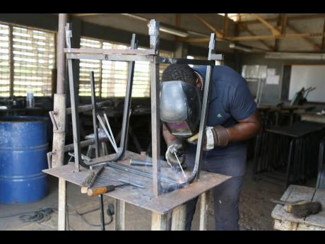 In this August 17, 2022, photograph, Burchell Simmonds, head of the Engineering Department at Vere Technical High School in Clarendon, welds a desk under the Ministry of Education and Youth programme to provide furniture for schools.