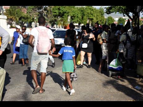 A man walks with a child on their way to board a taxi in downtown Kingston last Thursday. Several persons travelling with young children found it difficult to get transportation as drivers feared being fined for not having the children in car seats.