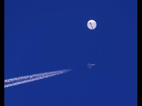 In this photo provided by Chad Fish, a large balloon drifts above the Atlantic Ocean, just off the coast of South Carolina, with a fighter jet and its contrail seen below it.