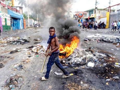 A man walks past a burning barricade during a protest against Haitian Prime Minister Ariel Henry calling for his resignation, in Port-au-Prince, Haiti, October 10, 2022.  Protests and looting have rocked the already unstable country since September 11, whe