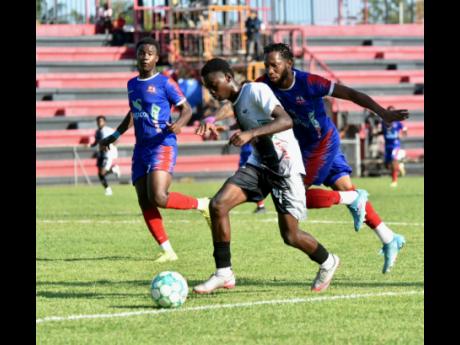 Omario Henry (centre) of Cavalier dribbles away from Odane Samuels (right) of Dunbeholden during their Jamaica Premier League encounter at the Anthony Spaulding Sports Complex yesterday.  Cavalier won 3-1. 