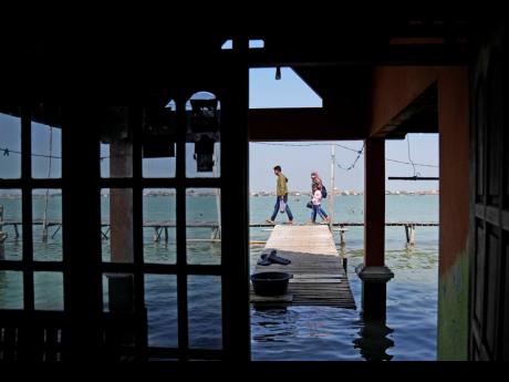 In this July 2022 photo, a family walks through Timbulsloko, Central Java, Indonesia. Rising seas in Timbulsloko have led people to raise the floors in their homes. 