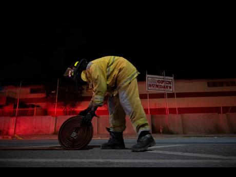 A firefighter rolls up a water hose during the Jamaica Fire Brigade’s response to a fire in Kingston in December 2022.