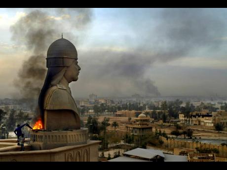 Smoke billows from the base of a sculpture depicting former Iraqi President Saddam Hussein after looters set it on fire atop the roof of his al-salam presidential palace in Baghdad in April 2003. 