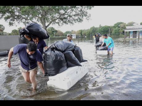 People try and save valuables, wading through high flood waters in a Fort Lauderdale, Fla., neighborhood on Thursday, April 13, 2023. South Florida is keeping a wary eye on a forecast that calls for rain a day after nearly a foot fell in a matter of hours.