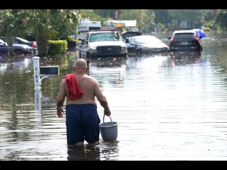 A man walks with a bucket on a flooded street, Friday, April 14, 2023, in Fort Lauderdale, Fla. South Florida has begun draining streets and otherwise cleaning up after an unprecedented storm that dumped upward of 2 feet of rain in a matter of hours. 