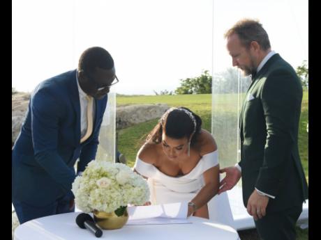 Credit: Ashley Anguin Tanisa signs her marriage licence and certificate as her husband Philipp (right) and Reverend Conrad Thomas look on.
