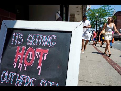 With temperatures hovering in the mid-90s, people walk near a sign down Hanover Street in the North End, Boston, during a summer heatwave in July 2022.
