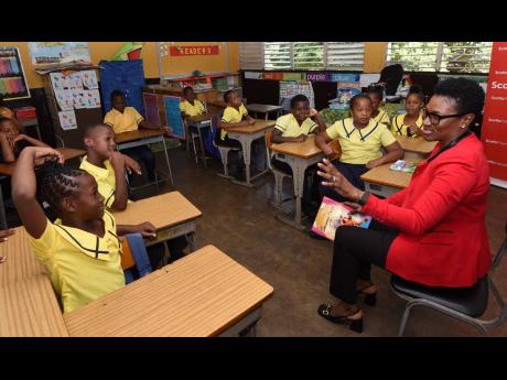 Audrey Tugwell-Henry (right), CEO of the Scotia Group, reads to grade-three students at Elletson Primary and Infant School during Read Across Jamaica Day on Tuesday.
