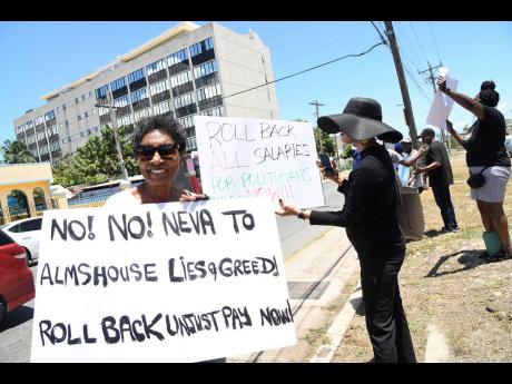 Kay Osborne (left) and other demonstrators bear placards as they protest a massive salary hike for the political directorate across the street from the Ministry of Finance and the Public Service in Kingston yesterday.