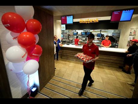 An employee of the Rostic’s restaurant in Tverskaya street carries food while celebrating opening ceremony in Moscow, Russia, Tuesday, April 25, 2023.