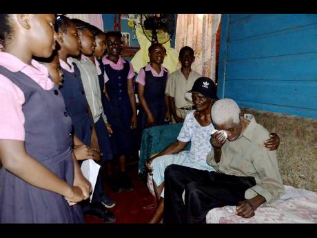 Centenarian Edwin McFarlane (right) wipes away  tears of joy as students of Sudbury Primary and Infant School in St James serenade him at his 100th birthday celebration. He is comforted by wife, Mavis McFarlane.