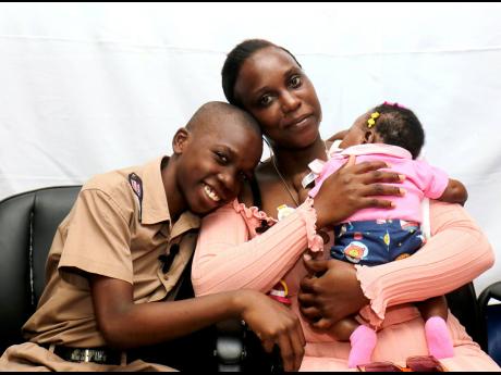 Eleven-year-old Donfarrel Lawrence and his mother Derron Buchanan smiles, while she holds his baby sister, at Corinaldi Avenue Primary School in Montego Bay, St James, on Monday. All had reason to be proud as Lawrence earned a place at Cornwall College bec