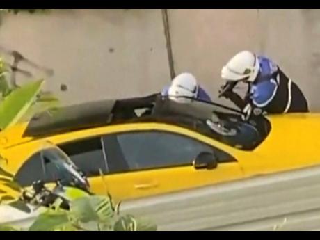 In this grab taken from video provided by @Ohana_FNG, two police officers question a driver, one pointing a gun towards the window of a yellow car, in Nanterre, France, on Tuesday, June 27. France’s government has announced heightened police presence aro