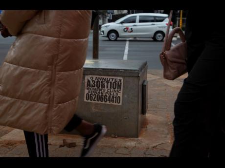 Women pass a sticker advertising abortion pills on a sidewalk in Johannesburg, June 28. 