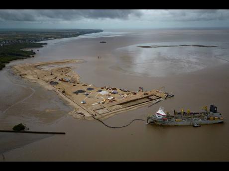 A ship creates an artificial island by extracting offshore sand to make a coastal port for offshore oil production at the mouth of the Demerara River in Georgetown, Guyana.
