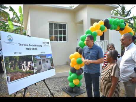 Prime Minister Andrew Holness (left), and New Social Housing Programme (NSHP) beneficiary, Barbara Johnson (centre), and Manchester North Western Member of Parliament, Mikhail Phillips, view pictures of her burnt out house in St Paul’s, Manchester, and t