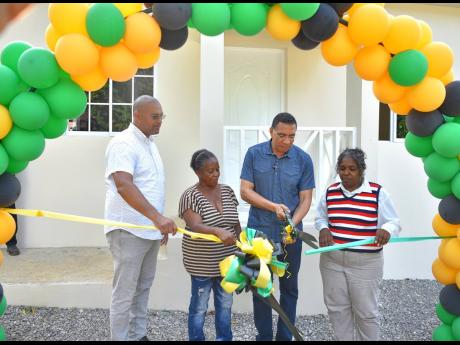 Prime Minister Andrew Holness (second right) cuts the ribbon prior to formally presenting the keys for a new three-bedroom house to resident of St Paul’s, Manchester, Barbara Johnson (second left). The home was built under the New Social Housing Programm
