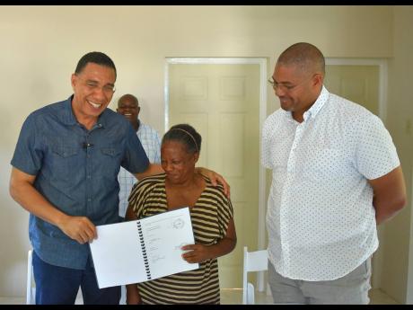 Prime Minister Andrew Holness (left) displays the document formalising New Social Housing Programme (NSHP) beneficiary, Barbara Johnson’s ownership of a three-bedroom home built in St Paul’s, Manchester, under the NSHP. Holness presented the keys to Jo