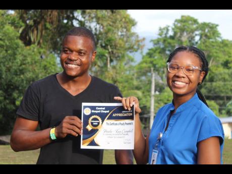 Volunteer Paula-Kay Campbell receives a certificate of participation from Pastor Ja’Vaughn Tayor of Central Gospel Chapel, where The Seven Eyes Stone Ministries recently hosted a health fair.