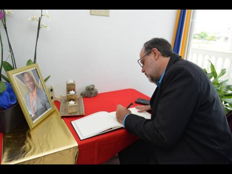 Opposition Leader Mark Golding signs the book of condolence for the late Ainsley Parkins at the Portmore Municipal Building in Portmore, St Catherine yesterday. 