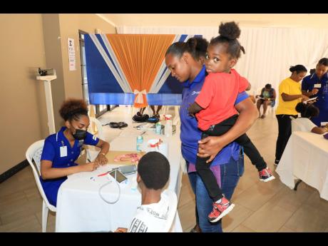 A mother (standing) watches as a UTech, Jamaica nursing student volunteer prepares to conduct medical screening on her son during the University of Technology, Jamaica, Back-to-School Community Health and Services Fair held at the Papine Campus on July 27,