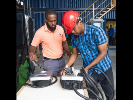 Delano Mighty (left), senior engineer for new business at Jamaica Energy Partners, watches as intern Zakhele Ellington carefully places a charger down during their morning test bench session.
